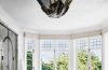 rounded bathroom with double windows in an arc at the back with a standalone marble tub at center and a floating marble vanity and a large bat like light fixture at center and a glass shower at left