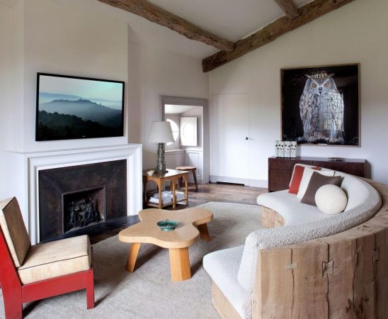 a seating area in a bedroom with a fireplace and curved sofa and red chair and large owl painting along the back wall